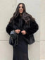 Woman wearing a black faux fur jacket over a black dress and holding a black purse.
