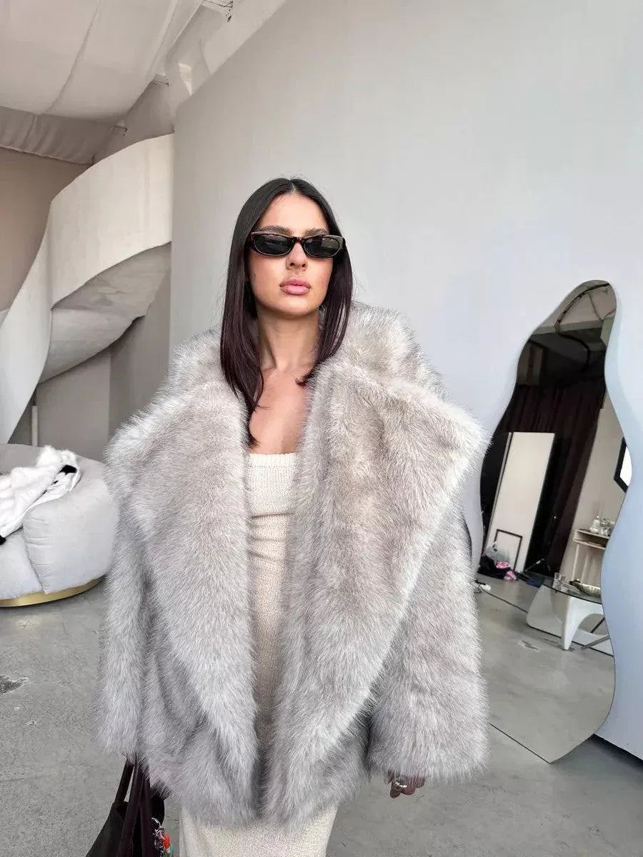woman in a light grey faux fur coat and cream dress posing indoors