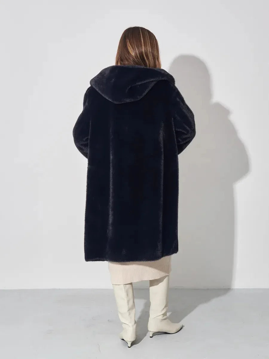 Woman wearing a black hooded faux fur coat, cream dress, and white boots, back view.