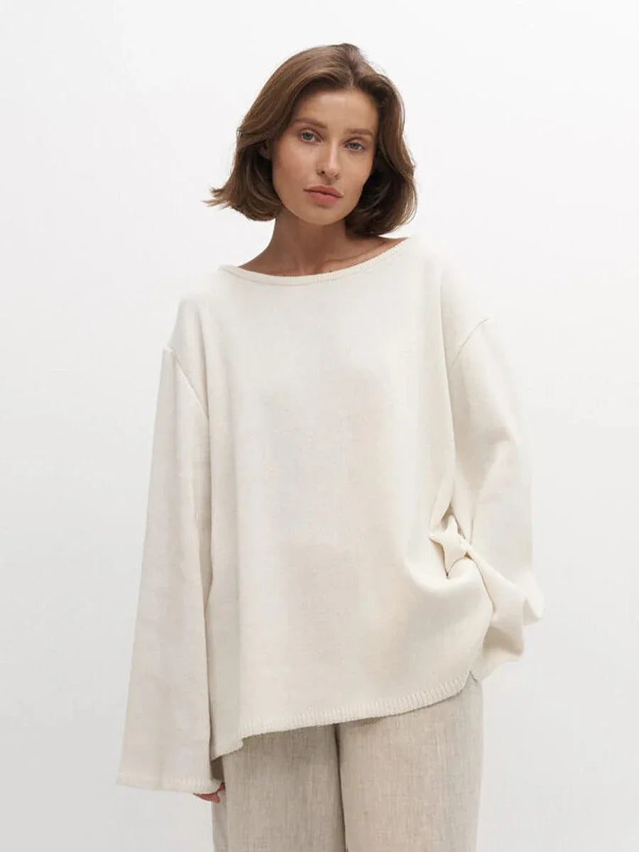 Close-up of a woman wearing an oversized cream knit sweater with a boat neck and beige pants.