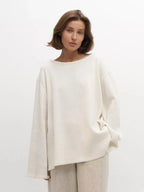 Close-up of a woman wearing an oversized cream knit sweater with a boat neck and beige pants.