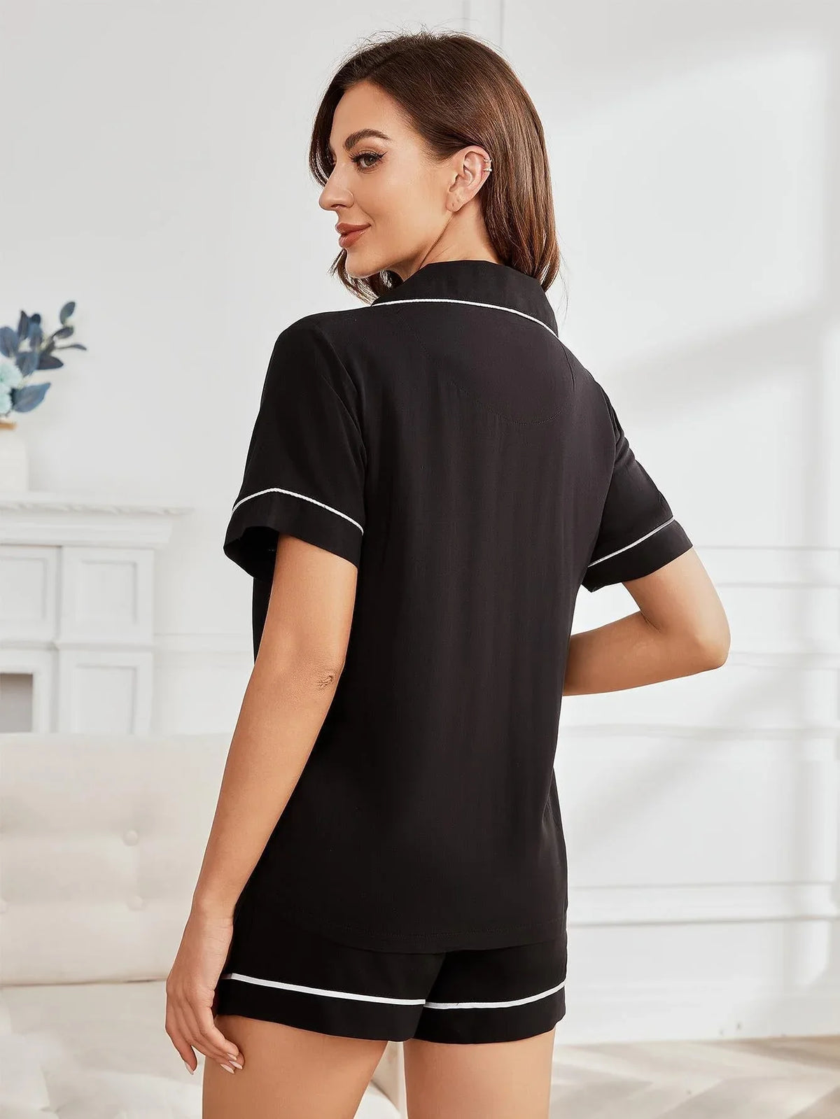 Woman from behind wearing a black short-sleeve pajama top with white piping.