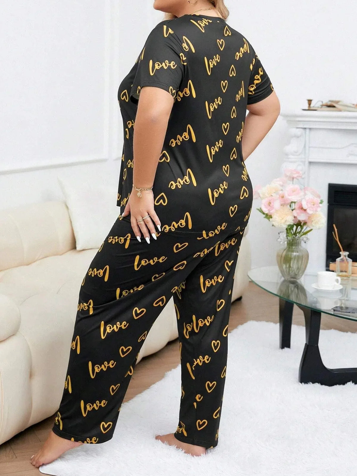 Woman wearing a black and gold "love" and heart print pajama set from the back.