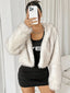 Woman wearing a white faux fur cropped jacket over a black dress, holding a phone.