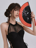 Close-up of a woman's face in a black one-piece swimsuit, holding a fan adorned with cherry blossoms
