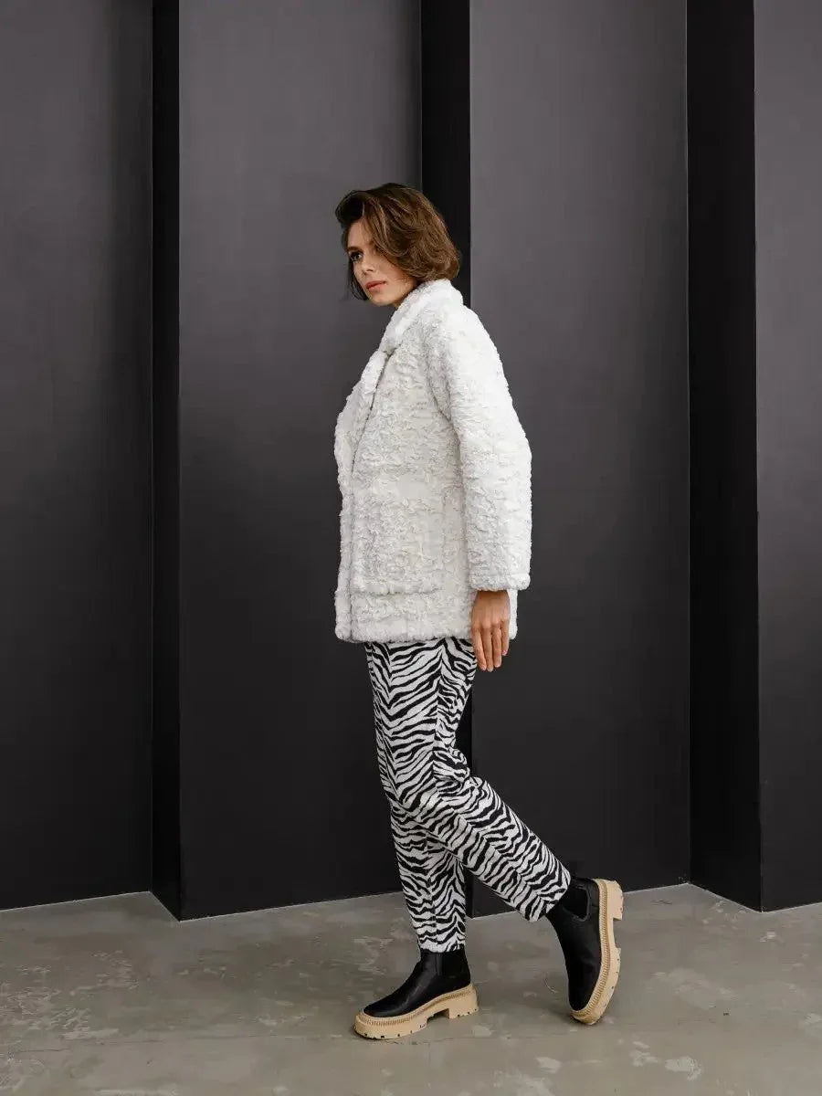 Side profile of a model walking in a white textured faux fur jacket and zebra print pants.