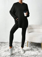 Woman in a black ribbed knit loungewear set, holding a coffee cup and resting hand on hip.