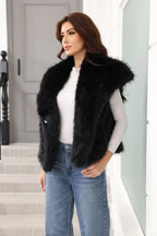 Woman wearing a black faux fur vest over a white long-sleeved shirt and blue jeans, with hands in pockets