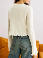 Detail of the ruffled hem on a white cropped cardigan.