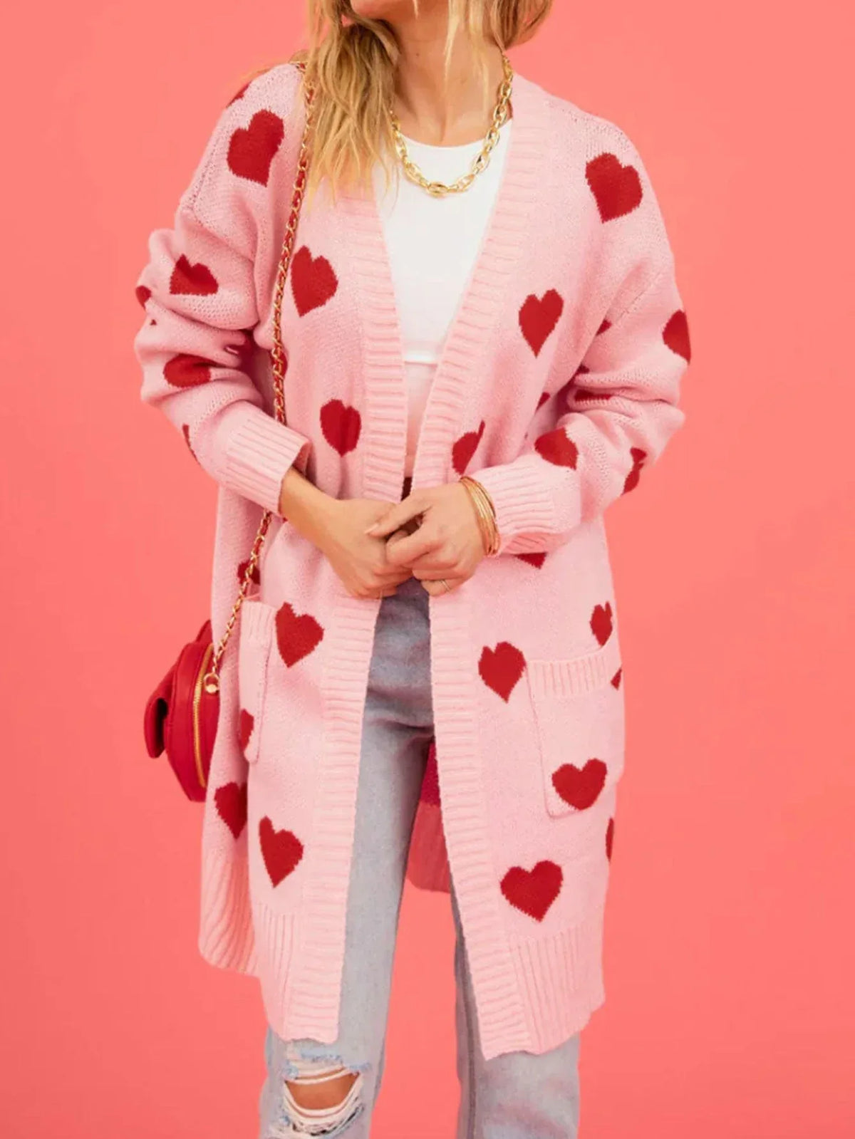 Woman wearing a pink longline cardigan with red hearts, paired with a white crop top and light wash jeans.