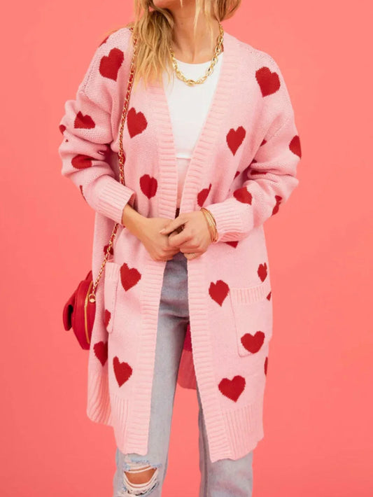 Woman wearing a pink longline cardigan with red hearts, paired with a white crop top and light wash jeans.