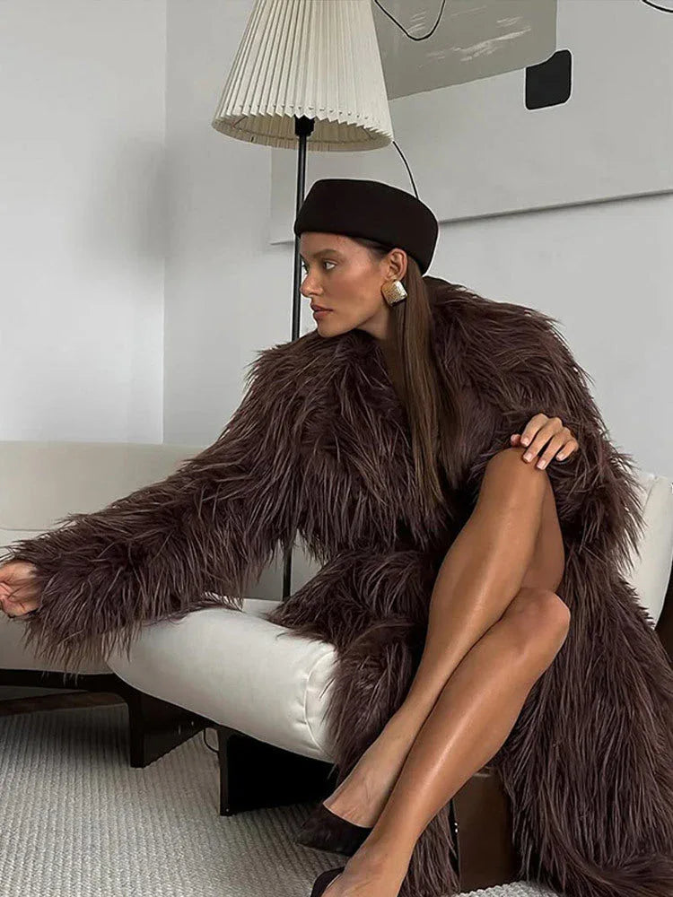 Woman sitting on a white sofa wearing a long brown furry coat and a brown beret