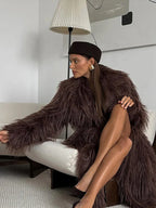 Woman sitting on a white sofa wearing a long brown furry coat and a brown beret