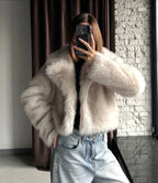 Close-up of a woman wearing a cream faux fur cropped jacket and light wash wide-leg jeans, holding a phone to take a mirror selfie.