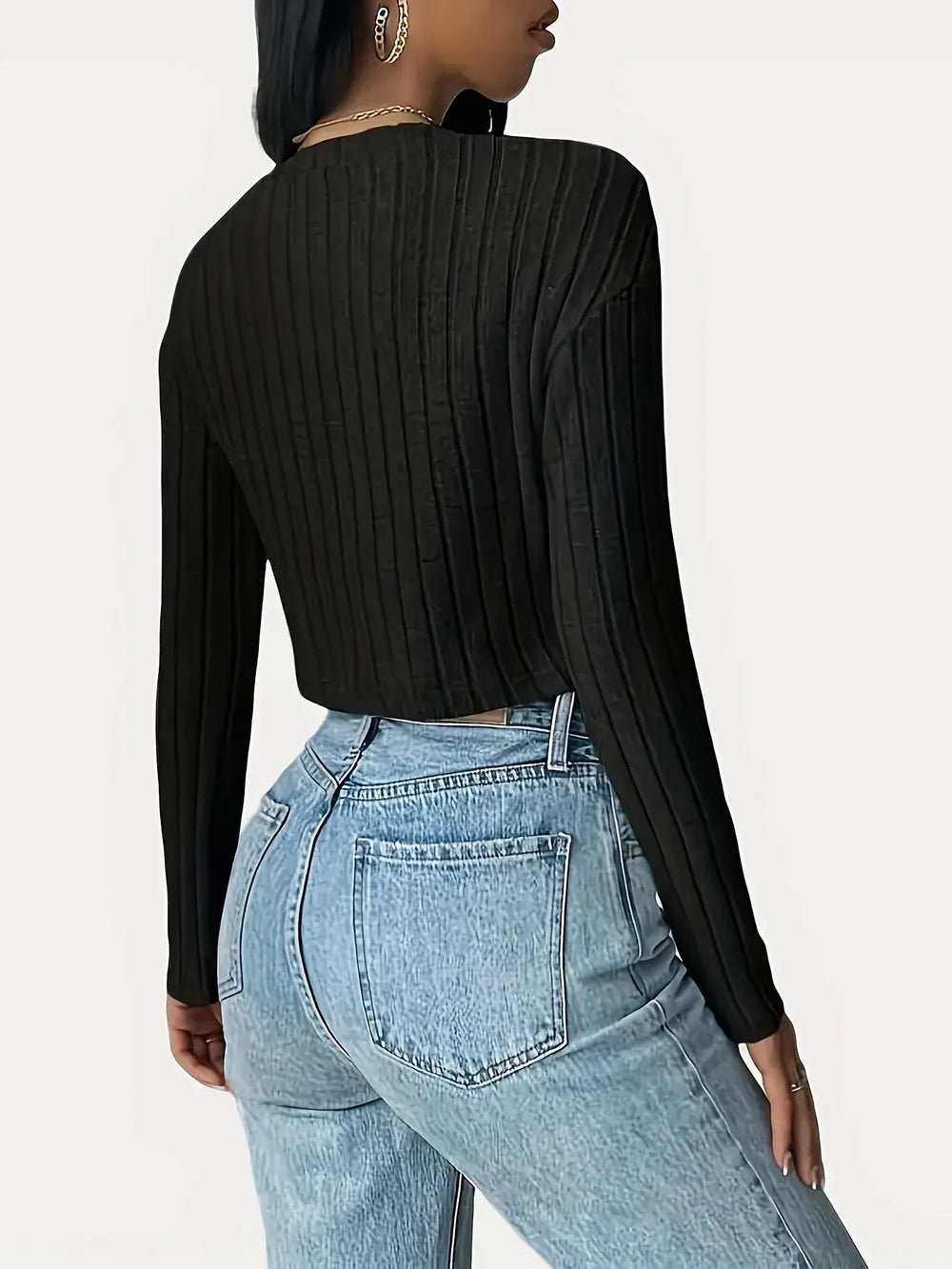 Back view of a woman wearing a black ribbed long-sleeve cropped top and light wash high-waisted jeans.