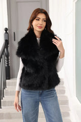 Woman wearing a black faux fur vest over a white long-sleeved shirt and blue jeans, standing on stairs