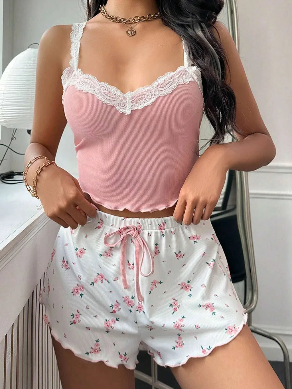 Woman in a pink ribbed knit camisole with white lace trim and floral print shorts in a mirrored setting