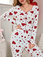 Close-up of a woman wearing a white long-sleeved pajama top with a red heart print and a bow detail.