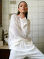 Woman wearing a white sheer knit sweater and white pants, posing in a bathroom setting.
