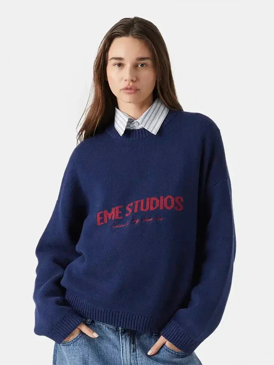 front view of a woman wearing a navy blue crew neck sweater with red "EME STUDIOS" embroidery
