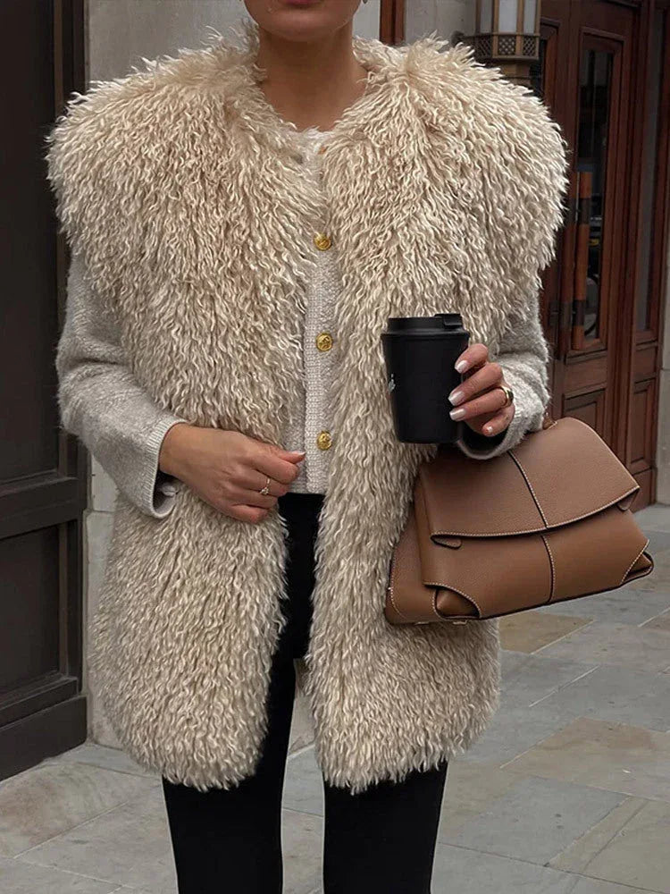 Close-up of a woman wearing a beige shaggy faux fur vest over a grey cardigan with gold buttons, holding a black coffee cup and a brown leather handbag.