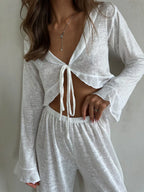 Front view of a woman wearing a white sheer knit crop top and wide-leg pants, showing the tie detail.