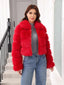Woman wearing a red faux fur cropped jacket with a grey turtleneck and blue jeans, standing on stairs.