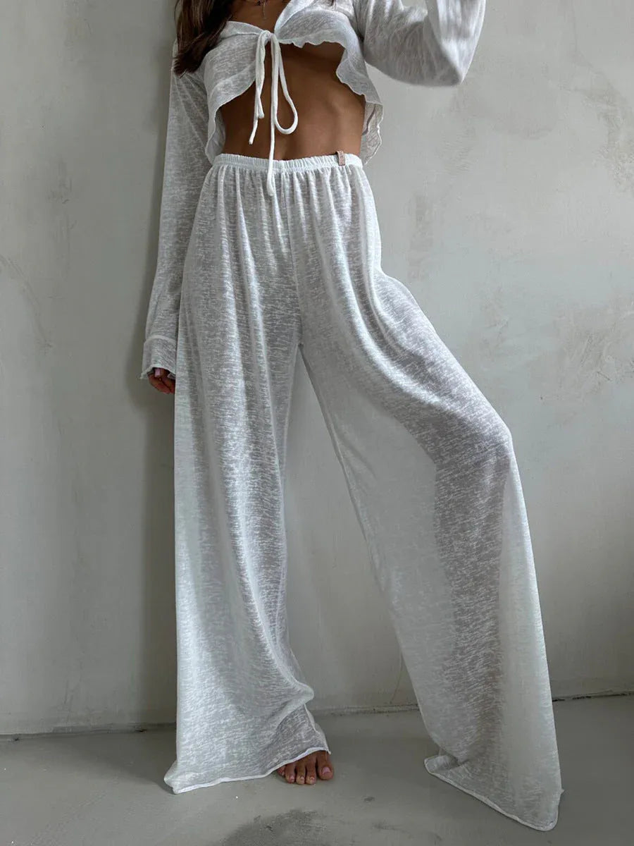 Close-up of a woman wearing a white sheer knit crop top and wide-leg pants.