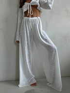 Close-up of a woman wearing a white sheer knit crop top and wide-leg pants.