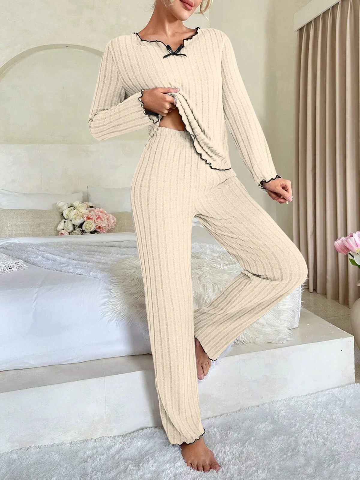 Woman standing wearing a cream ribbed knit pajama set with black trim. Main image