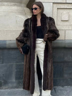 woman wearing a long brown fur coat with white pants and black accessories