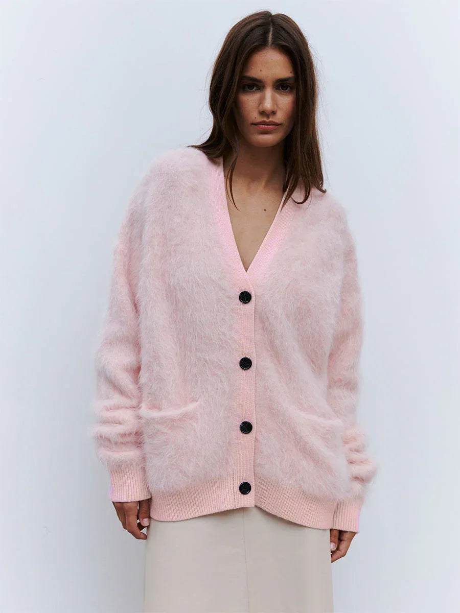 Woman wearing a pink fuzzy V-neck button-up cardigan with two front pockets and a cream skirt.