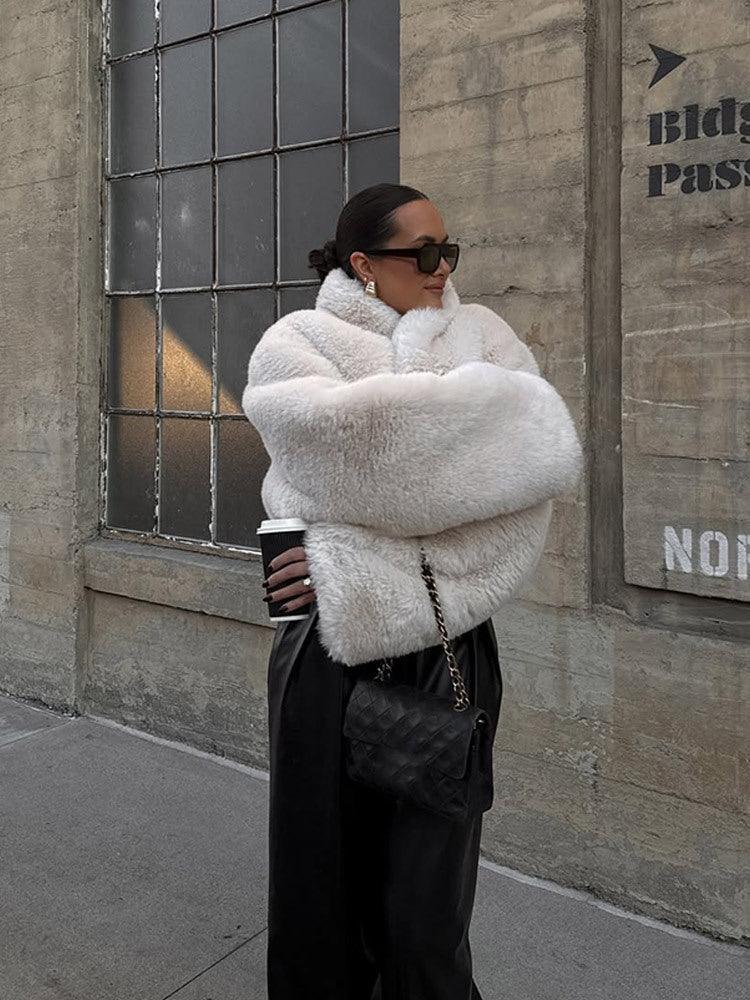 woman wearing a white faux fur jacket and black leather pants holding a coffee cup outdoors