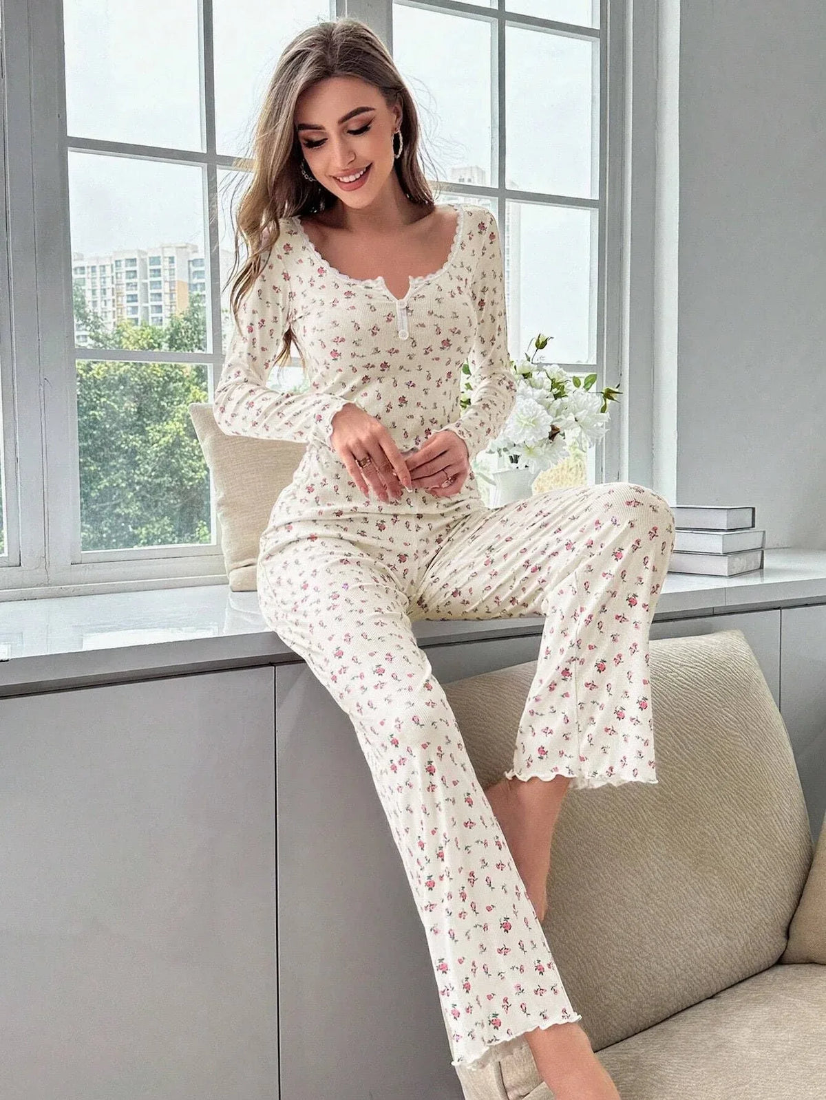 Woman smiling while sitting on a windowsill wearing a floral print pajama set
