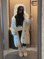 Woman wearing a long white faux fur coat, black outfit, and white moon boots, holding a white quilted handbag.