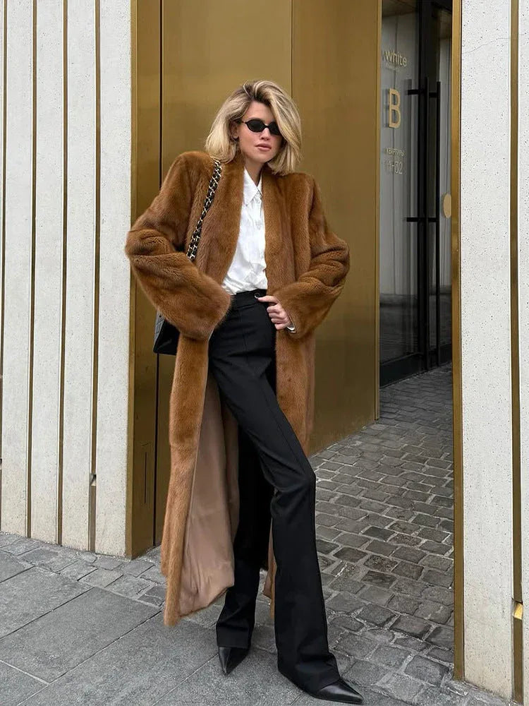 Woman wearing a long brown faux fur coat and black pants.