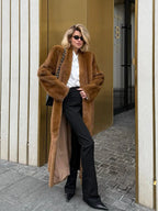 Woman wearing a long brown faux fur coat and black pants.