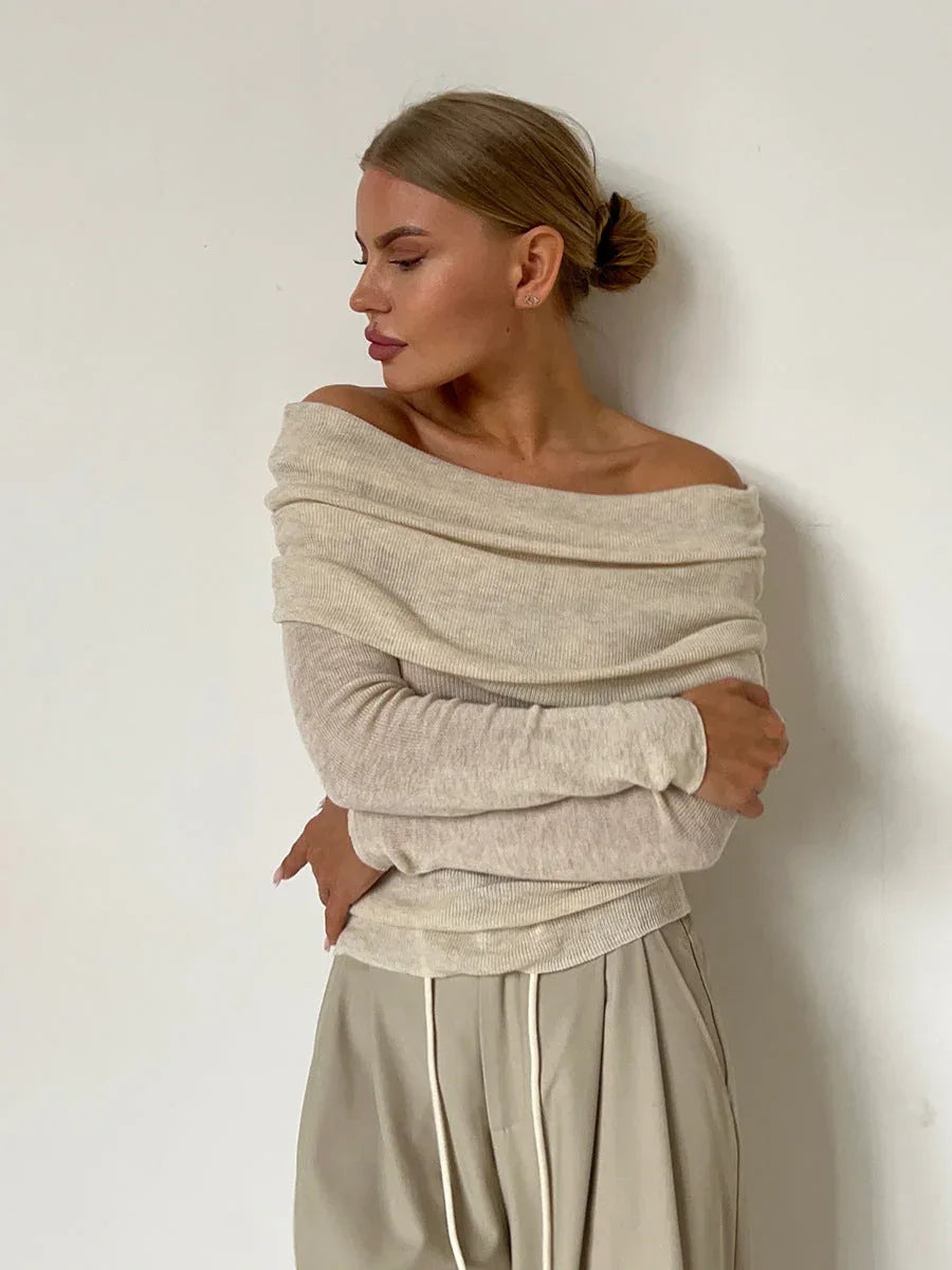 Woman wearing a cream off-the-shoulder ribbed knit sweater with long sleeves and beige wide-leg pants, standing against a white wall. Main image