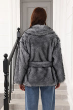 Back view of a woman in a grey faux fur jacket with a belted waist.