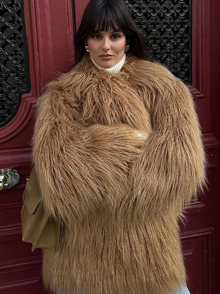 woman wearing a shaggy brown faux fur coat and a white turtleneck, with arms crossed