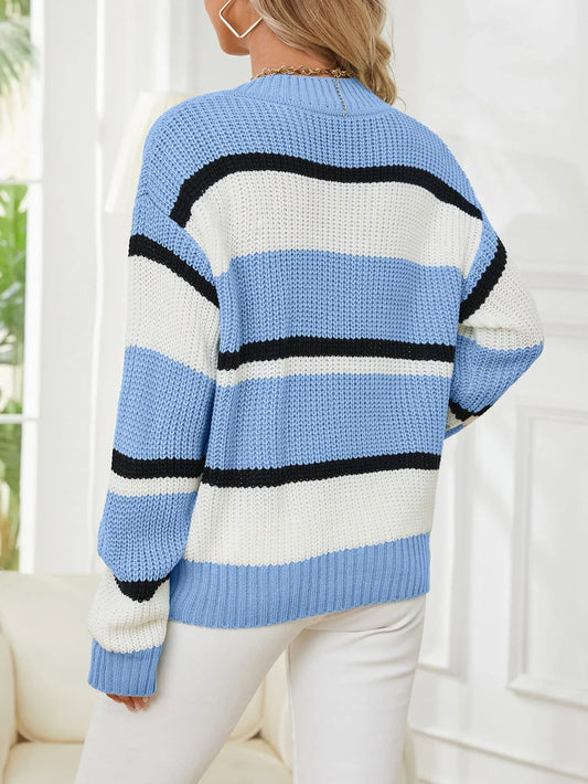 Back view of a woman wearing a blue, white, and black striped v-neck sweater with white pants.