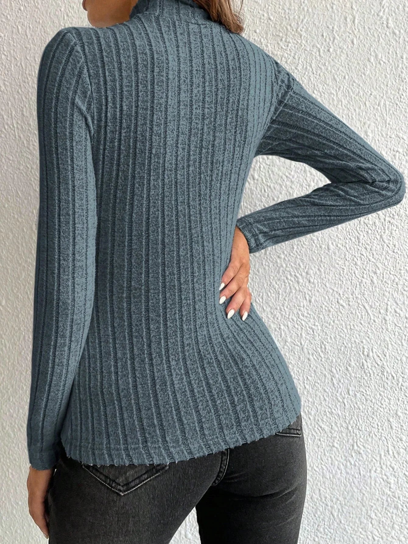 Back view of a woman wearing a fitted, long-sleeved, ribbed mock neck top in a blue-grey color with black jeans.