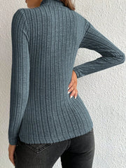 Back view of a woman wearing a fitted, long-sleeved, ribbed mock neck top in a blue-grey color with black jeans.