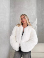 Woman in a white fluffy faux fur cropped jacket and dark wash jeans, smiling and looking at the camera.