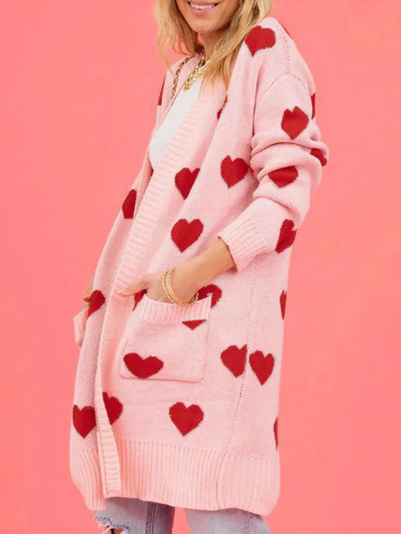 Close-up of a woman's hands in the pockets of a pink and red heart print cardigan.
