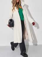 Model holding a black handbag and wearing a white faux fur coat