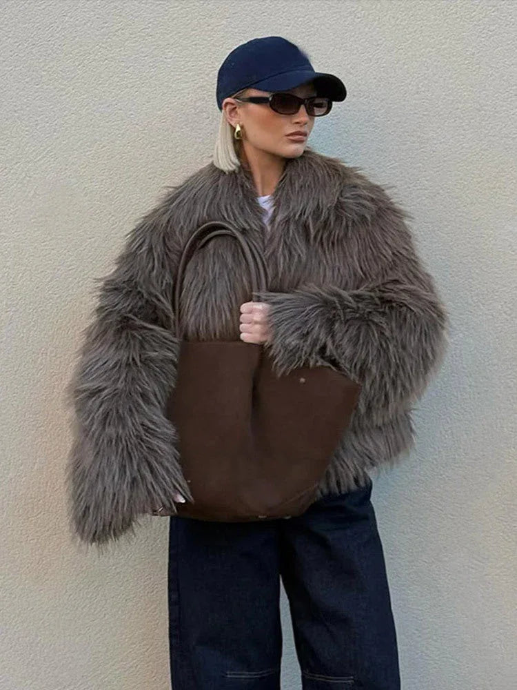 Woman wearing a shaggy grey faux fur jacket with dark wash wide-leg jeans, a navy baseball cap, sunglasses, and a brown tote bag. Main image
