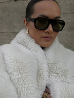 close-up of a woman wearing a white faux fur jacket and sunglasses