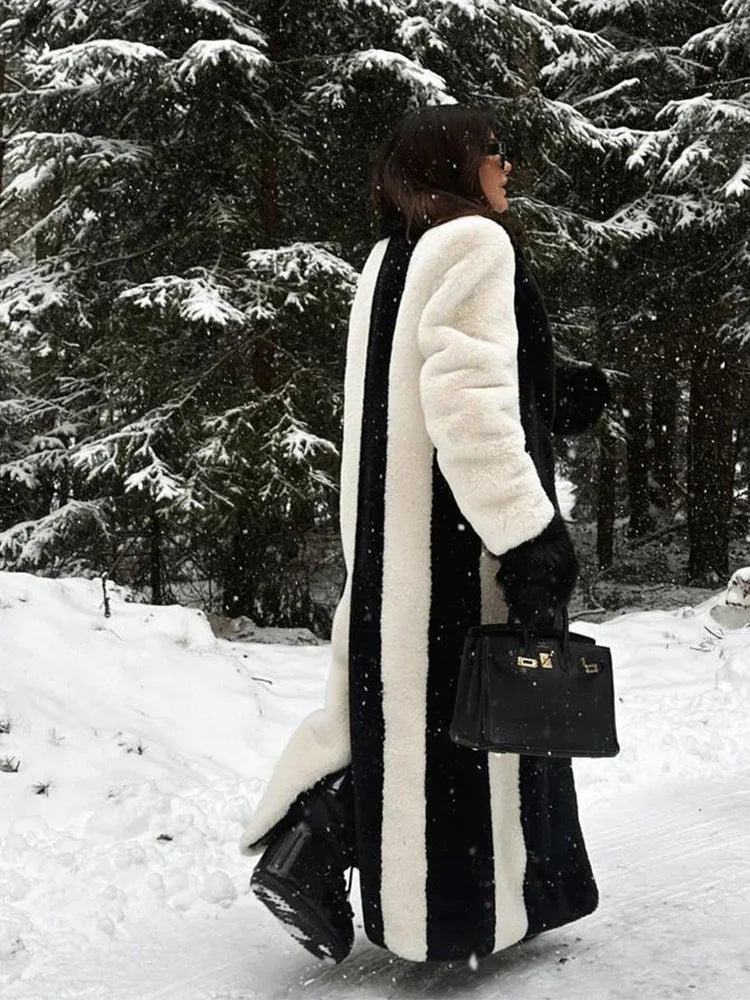 Rear view of a woman in a striking black and white vertical striped faux fur coat, walking in a snow-covered forest.