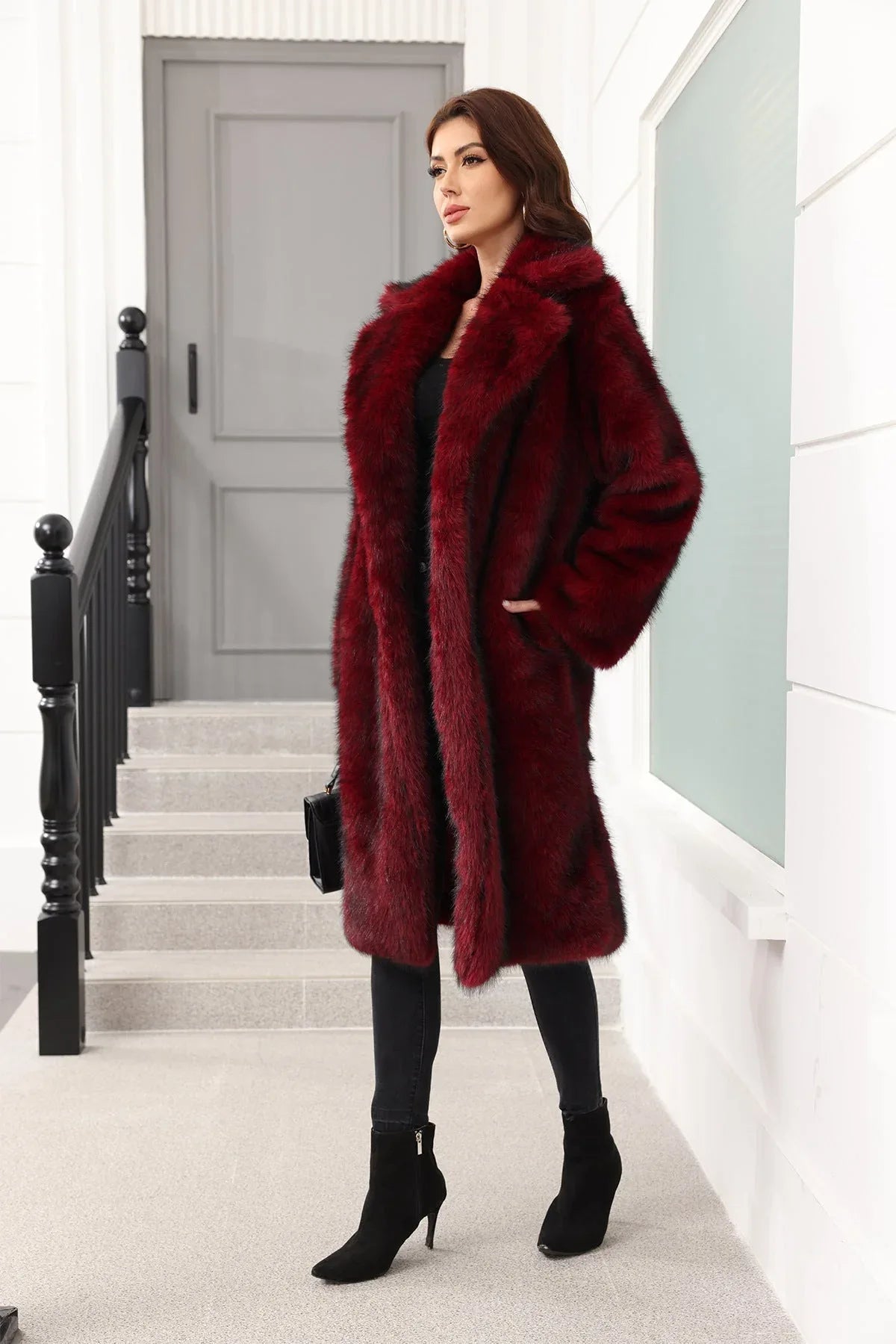 A woman wearing a long, burgundy faux fur coat over a black top and black pants, with hands in pockets.